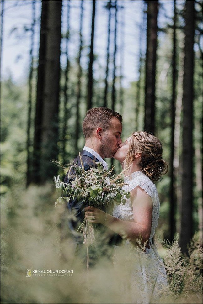 Newlyweds kissing among tall forest trees